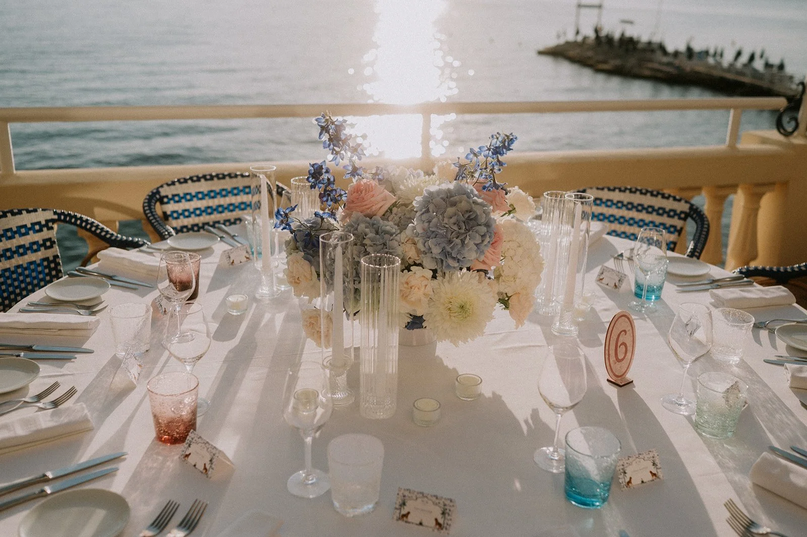 Round wedding table with a low hydrangea and garden rose centrepiece, numbered card and sea view, by wedding florist GRÖNT, French Riviera