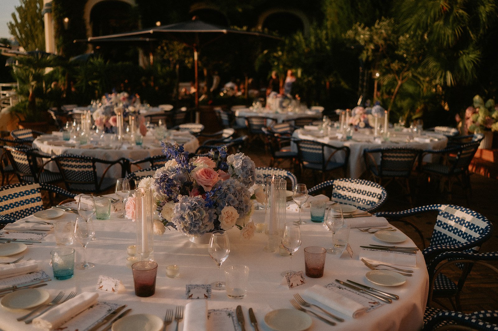 Reception tables on a Riviera terrace at golden hour with low hydrangea and rose centrepieces and candlelight, Antibes wedding