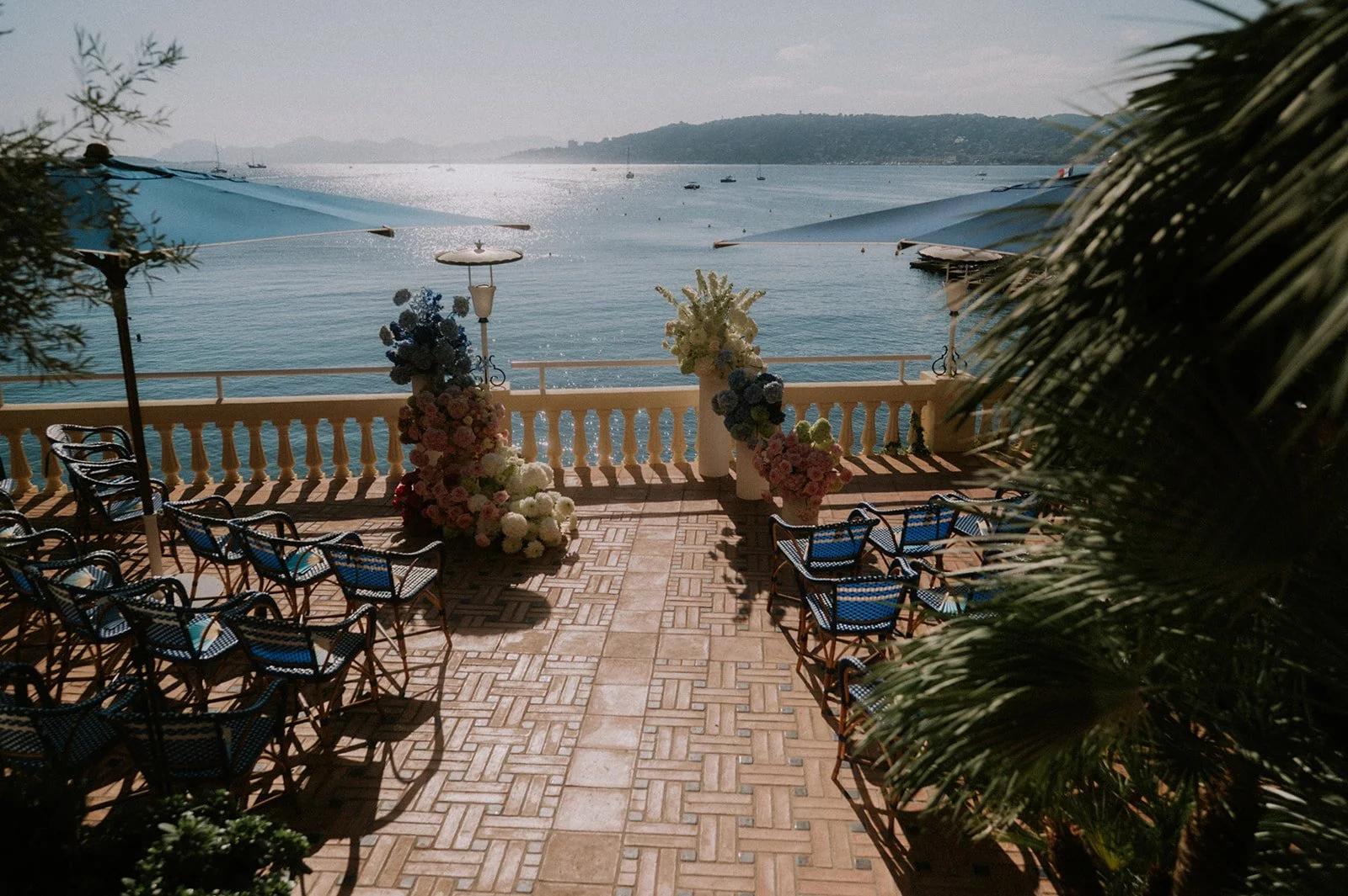 Antibes wedding ceremony terrace with blue umbrellas, seating and flower installations above the Mediterranean