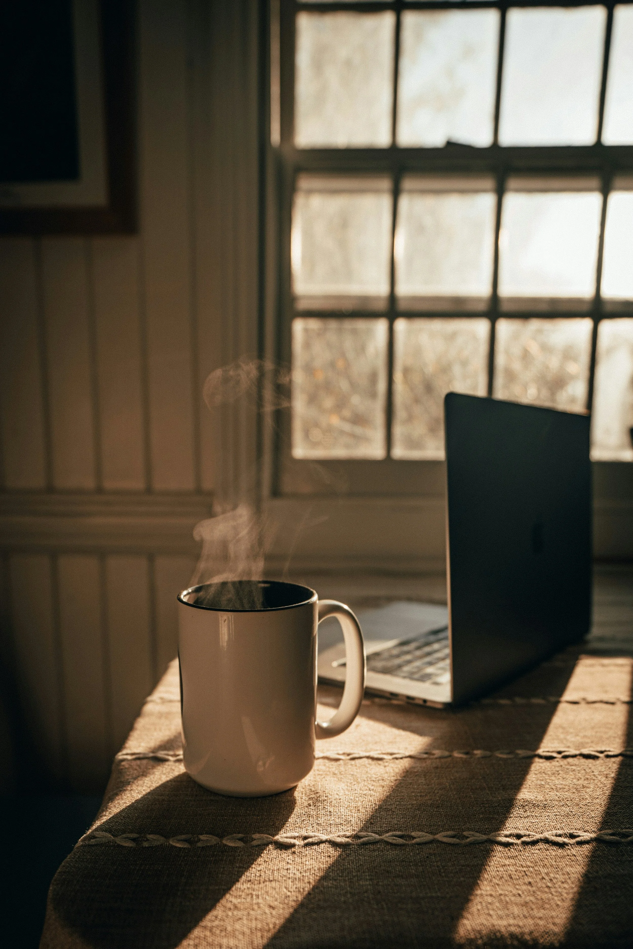 Laptop and steaming cup of coffee on a desk in a calm home setting