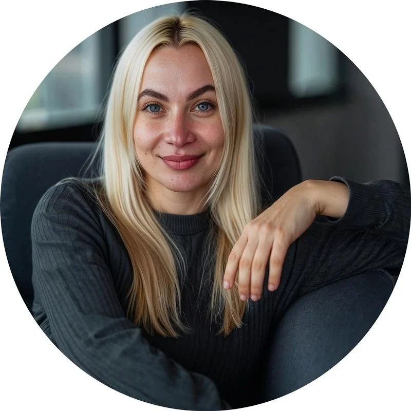 Frau mit blonden Haaren in einem dunklen Pullover sitzt auf einem Sofa und lächelt in die Kamera.