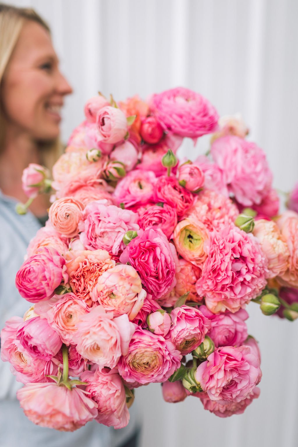 Jenny Marks of the Six Figure Flower Farming Podcast is holding a bouquet of pink ranunculus.