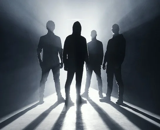 Silhouettes of four people standing with dramatic backlighting casting shadows.