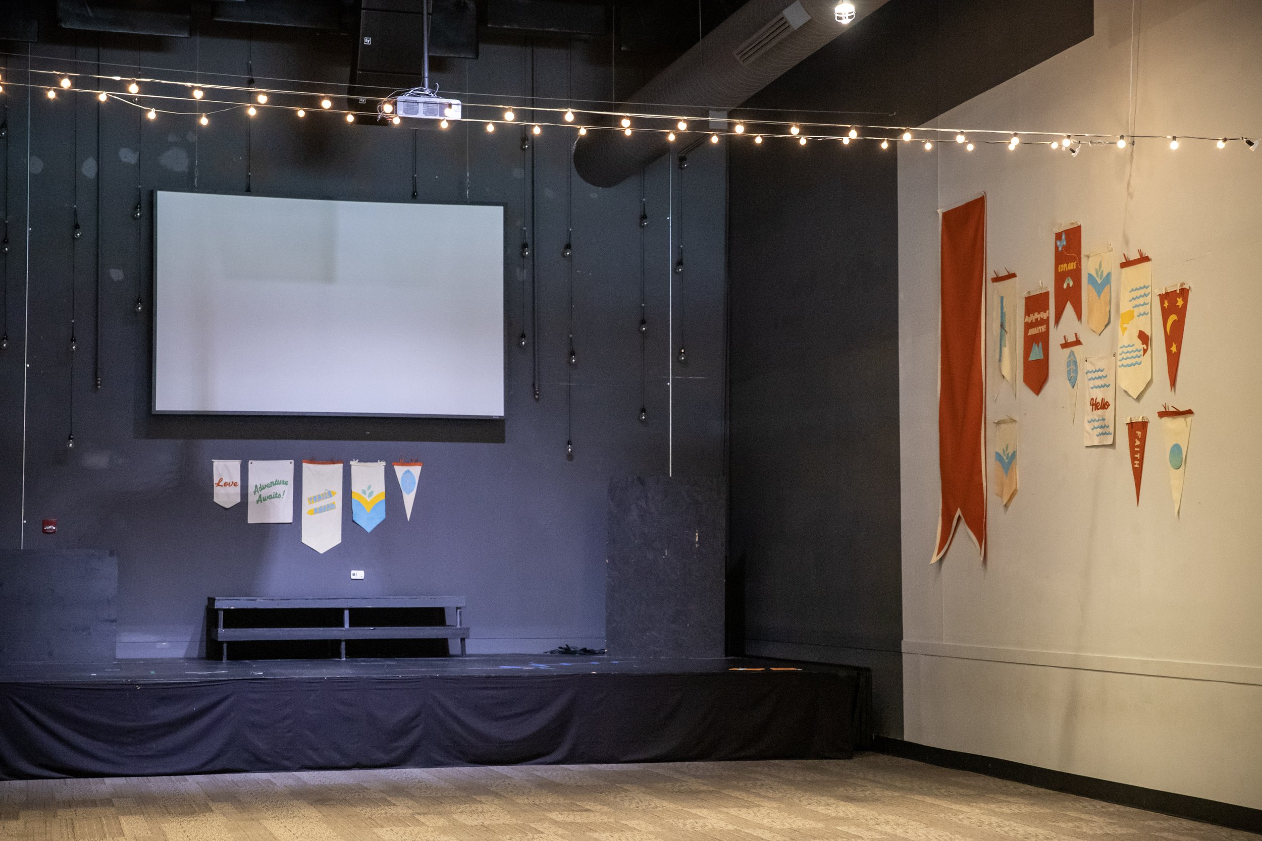 Empty stage with black backdrop, string lights hanging above, bunting with motivational words and decorations on the wall to the right in Richmond, VA.