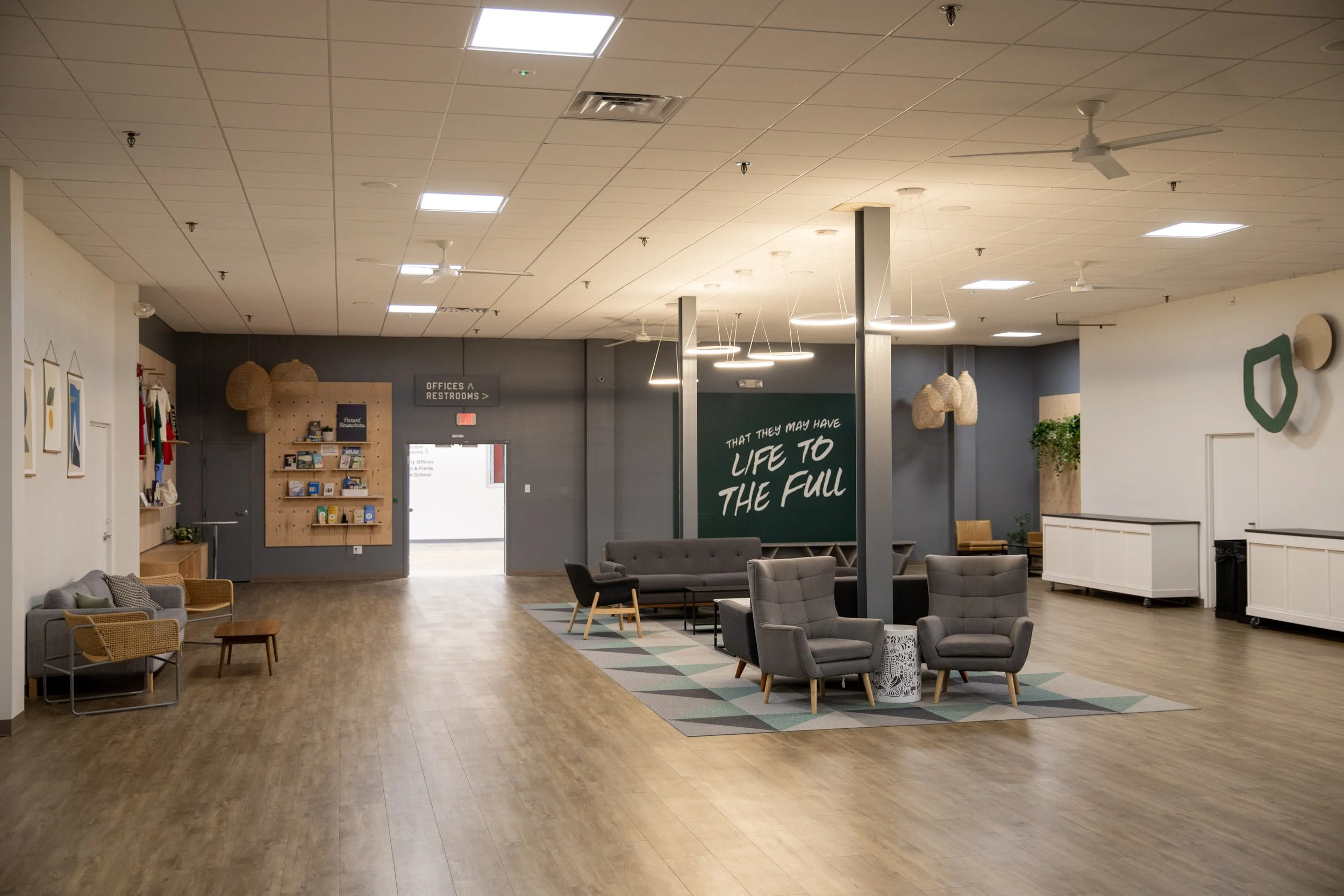 A spacious, modern lounge area with various chairs and sofas, a wooden floor, wall art, greenery, and lighting fixtures hanging from the ceiling in Richmond, VA.