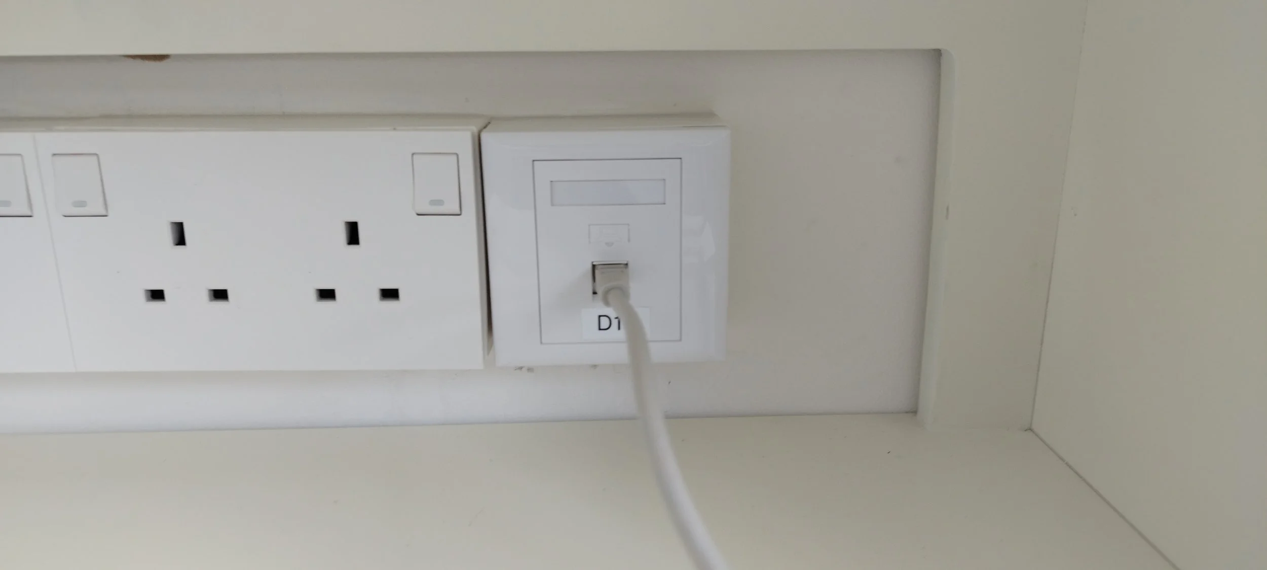 Electrical outlets and a power outlet with a connected white charging cable on a white wall.
