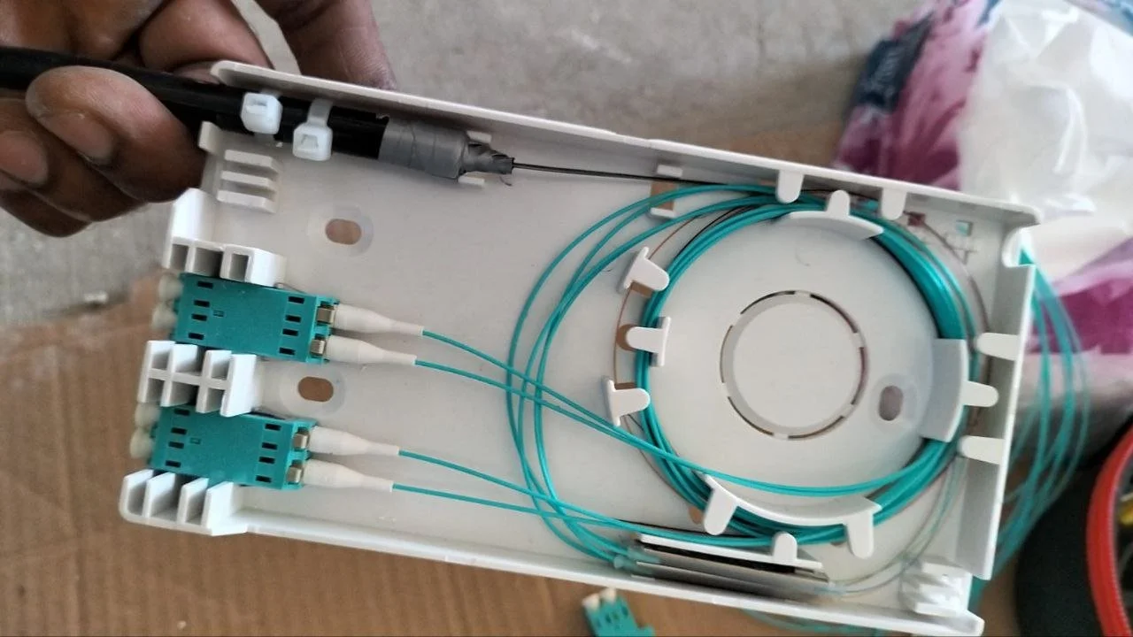 Close-up of a fiber optic splice tray with turquoise fiber optic cables, connectors, and splicing tools inside a plastic enclosure.