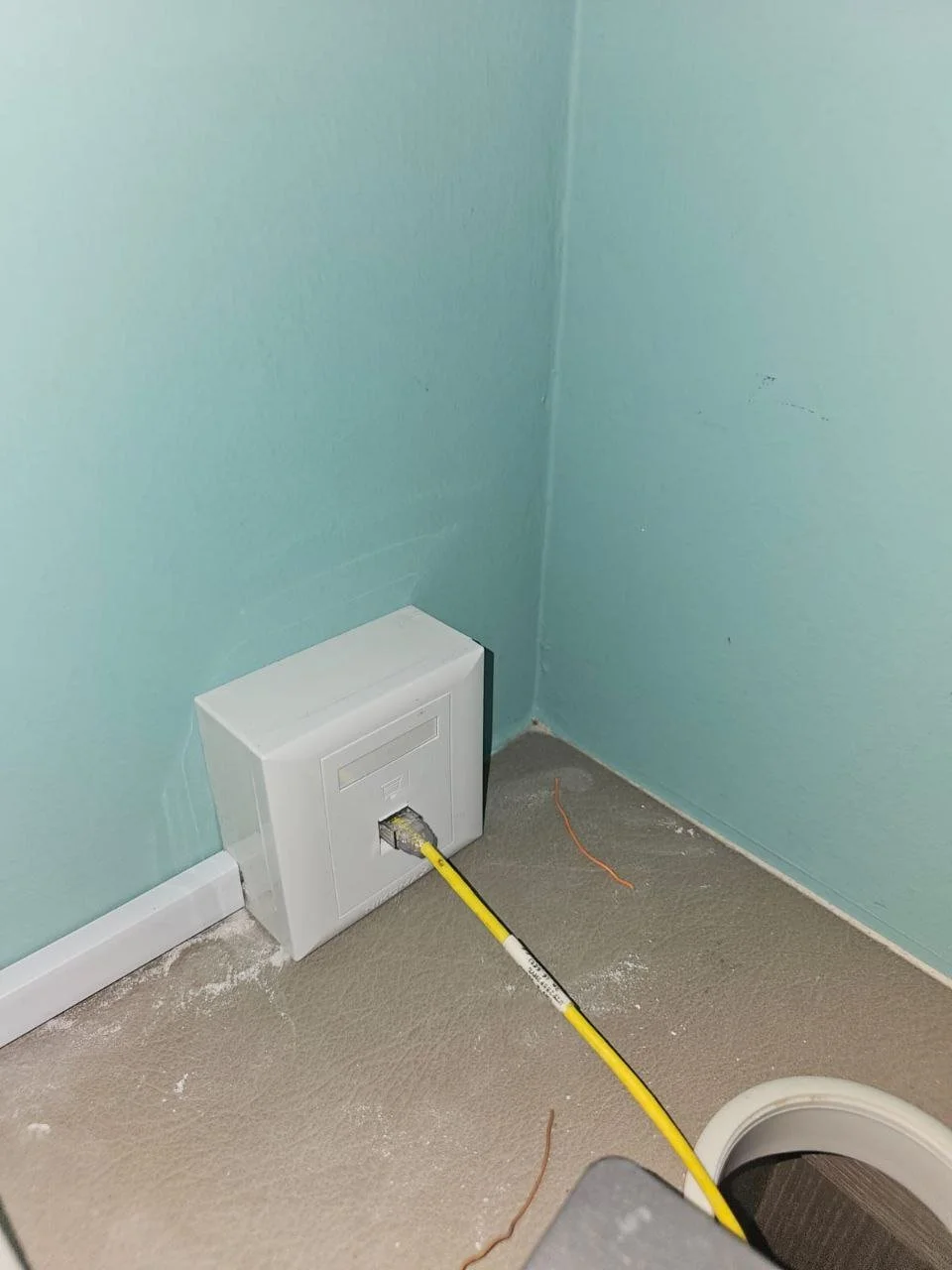 A network cable connected to a wall box in a room with unfinished flooring and light teal walls.