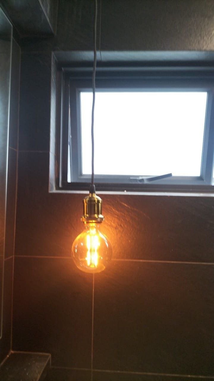A hanging Edison-style light bulb with a visible filament, lit and glowing in a room near a small window.