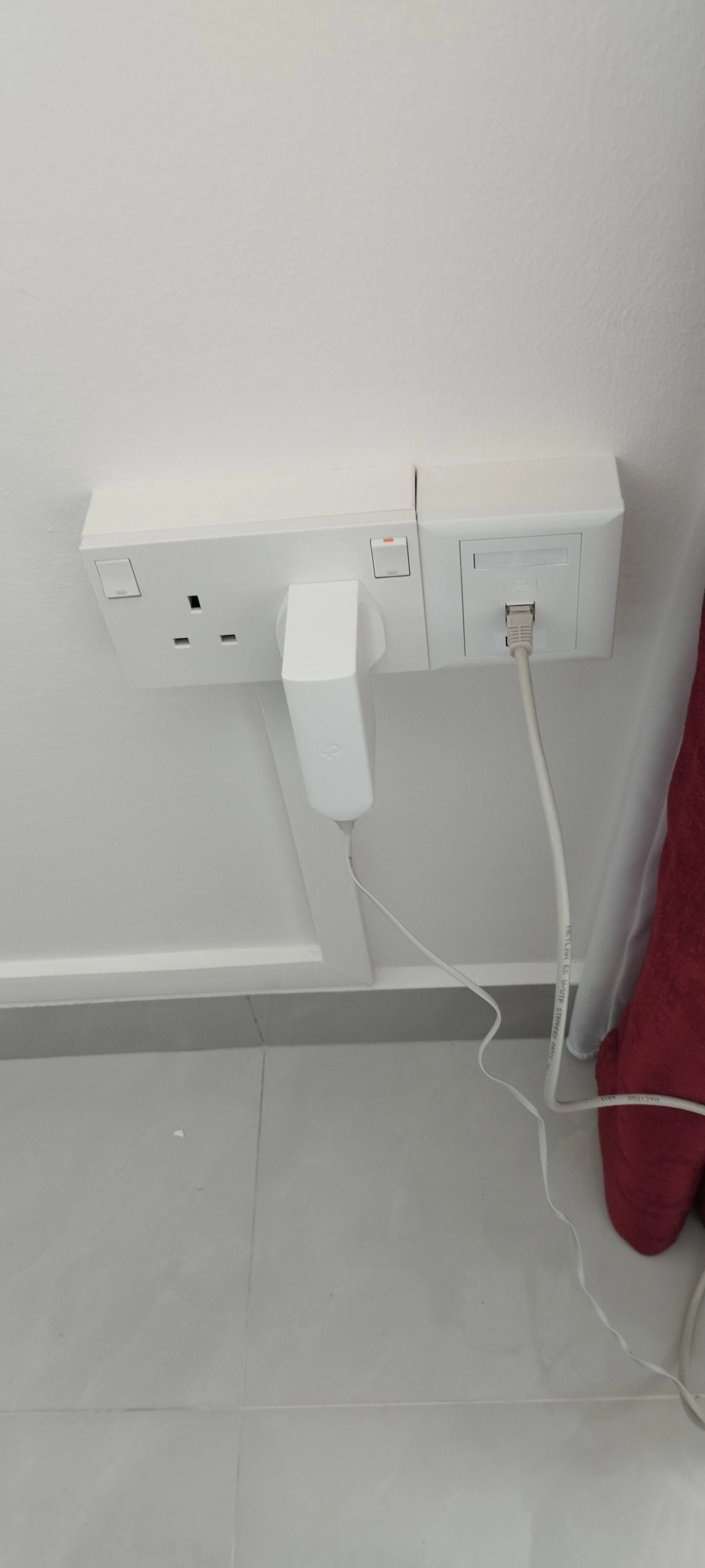 A wall with a UK electrical socket, a two-prong outlet, a white power strip with a hand-held electric shaver connected to it, and an Ethernet cable plugged into a network port.