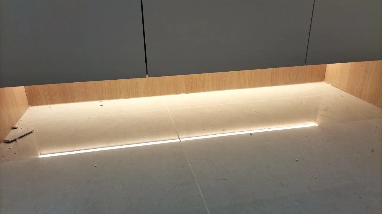 Modern interior space with grey cabinets, wooden paneling, and LED lighting near the floor.