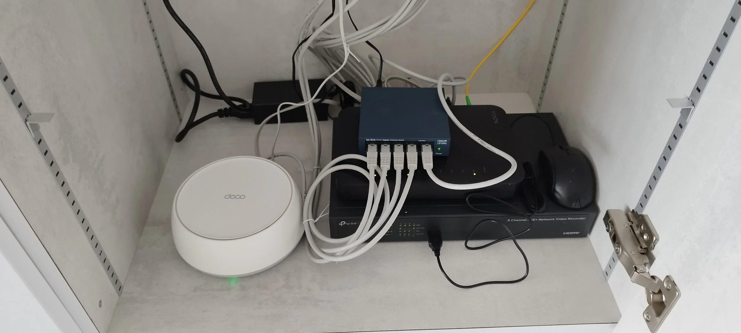 Networking equipment inside a cabinet including a white Daco device, a TP-Link gigabit network switch, a black network recorder, and various connected cables.