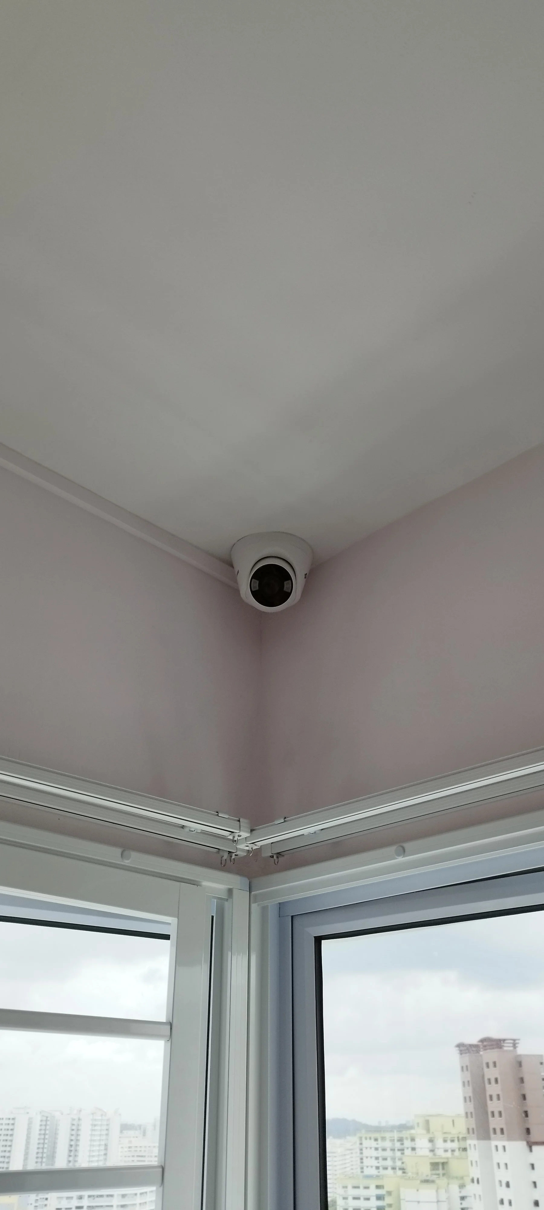 Security camera mounted in the corner near a window in a high-rise building, with a cityscape view outside.