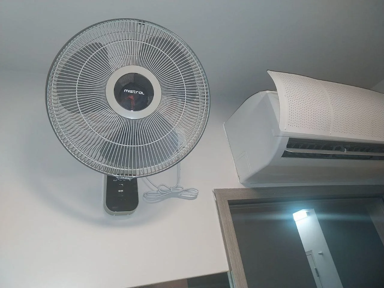 Wall-mounted fan and air conditioning unit in a room with a window.