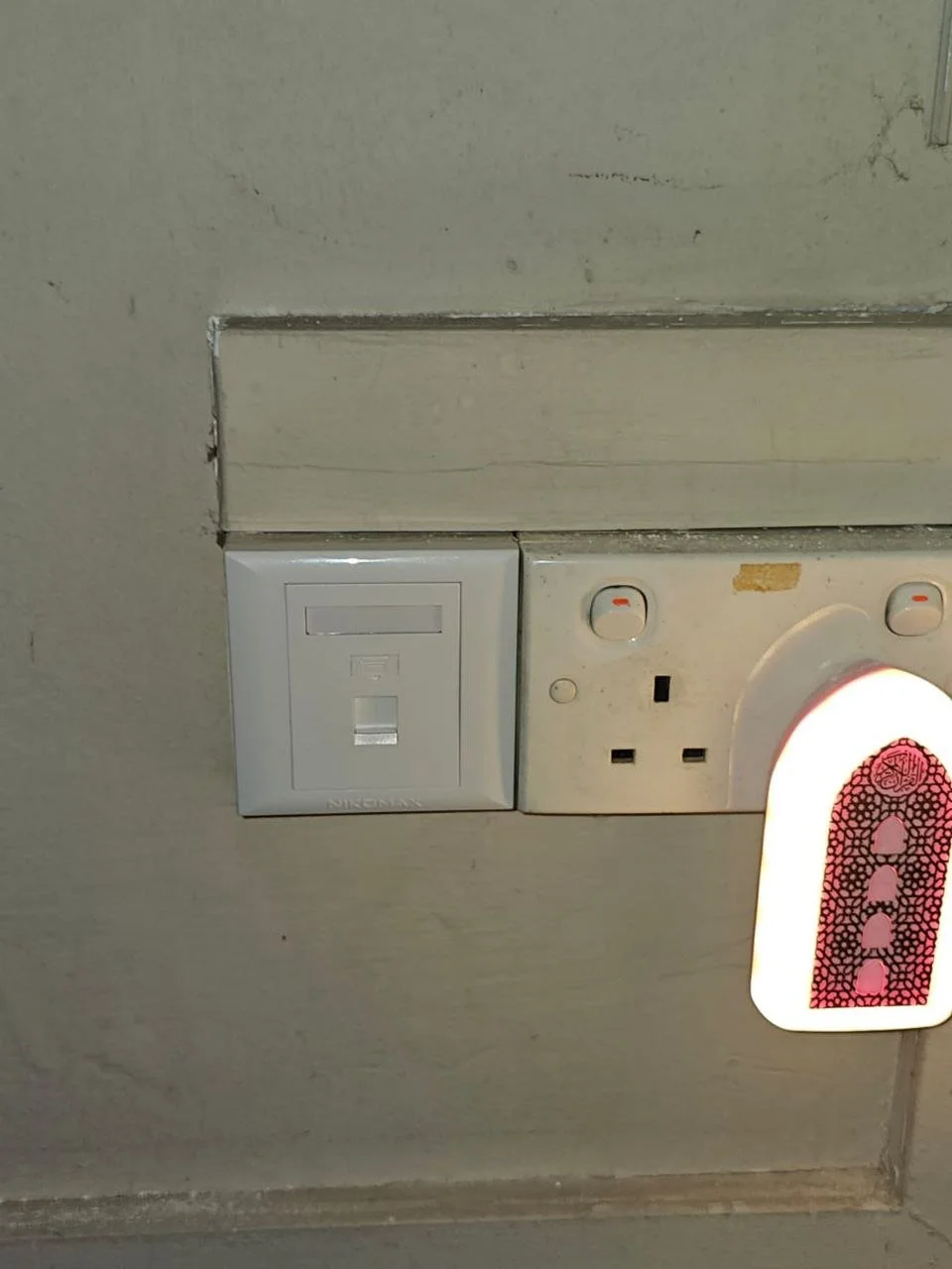 Close-up of electrical outlets and a nightlight on a wall, with some damage around the outlets.