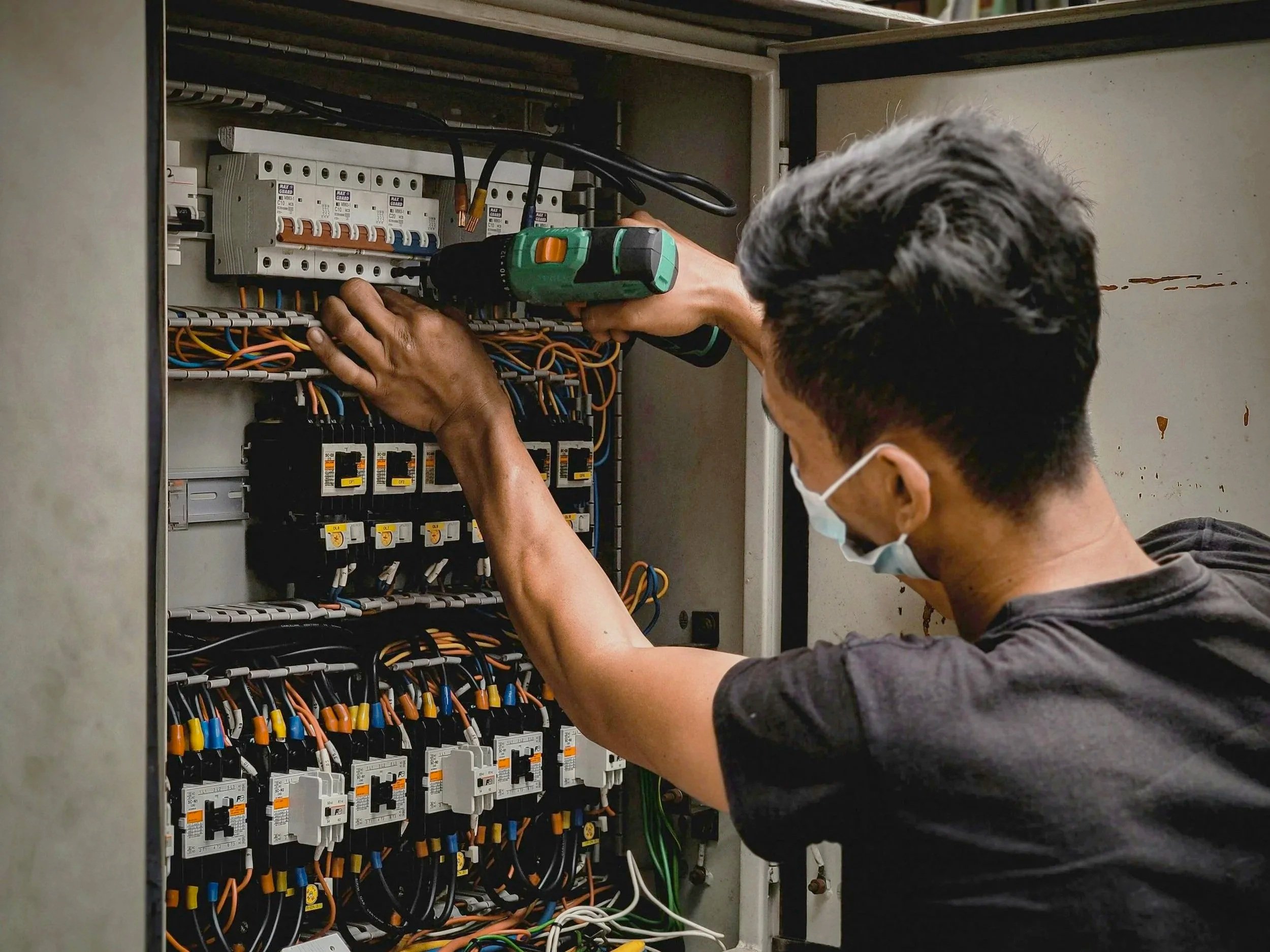 A technician working inside an electrical panel, using a cordless drill.