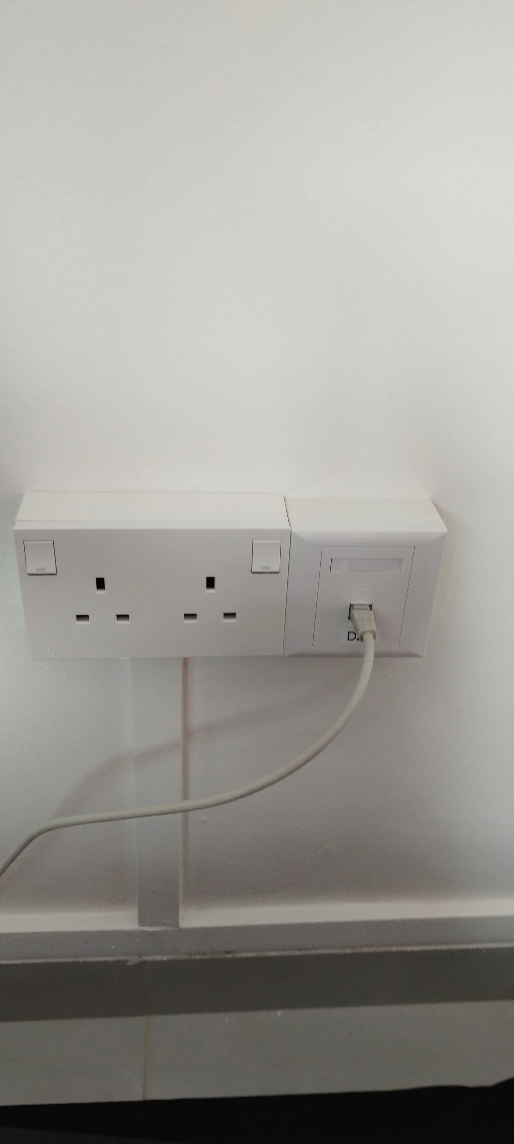 White electrical outlet and power socket on a white wall with a plugged-in white cable.