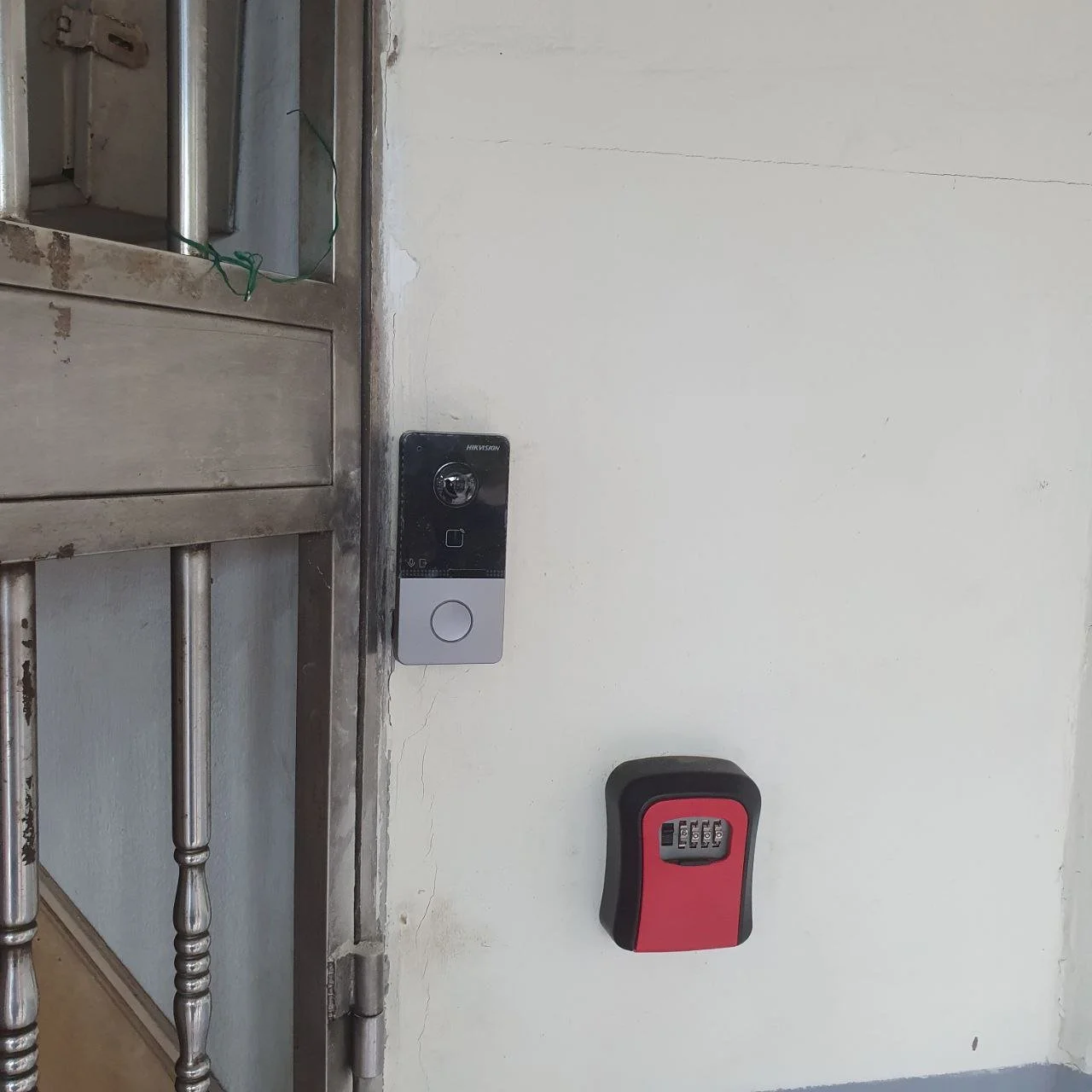 An outdoor security keypad and a card reader mounted on a white wall near a metal gate.