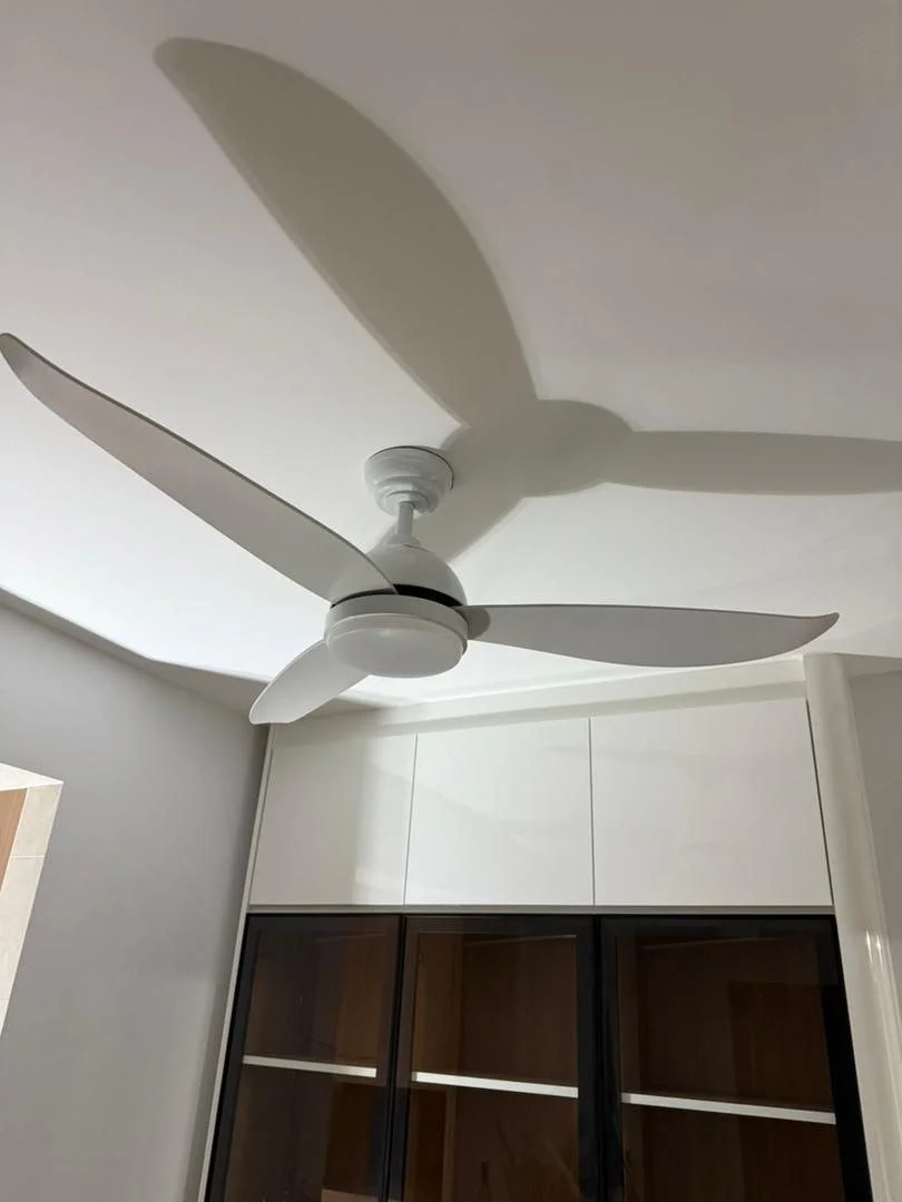 White ceiling fan with three blades casting a shadow on the ceiling in a room with white and dark wood cabinets.