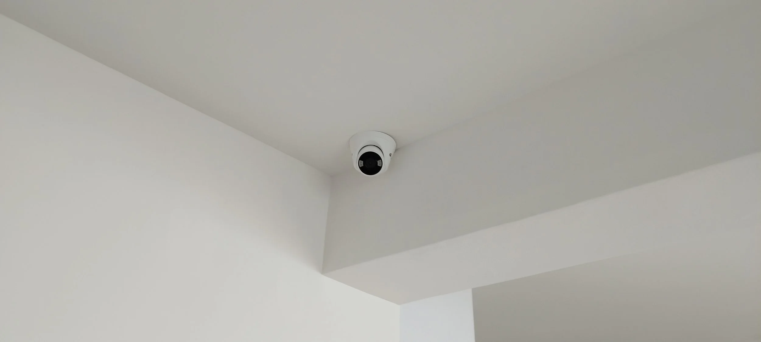 Security camera mounted on a white ceiling in a corner of a room.