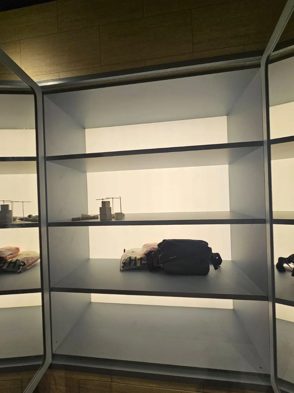 Empty retail display shelf with a black bag and some magazines or brochures, in a store with mirrors on the sides.