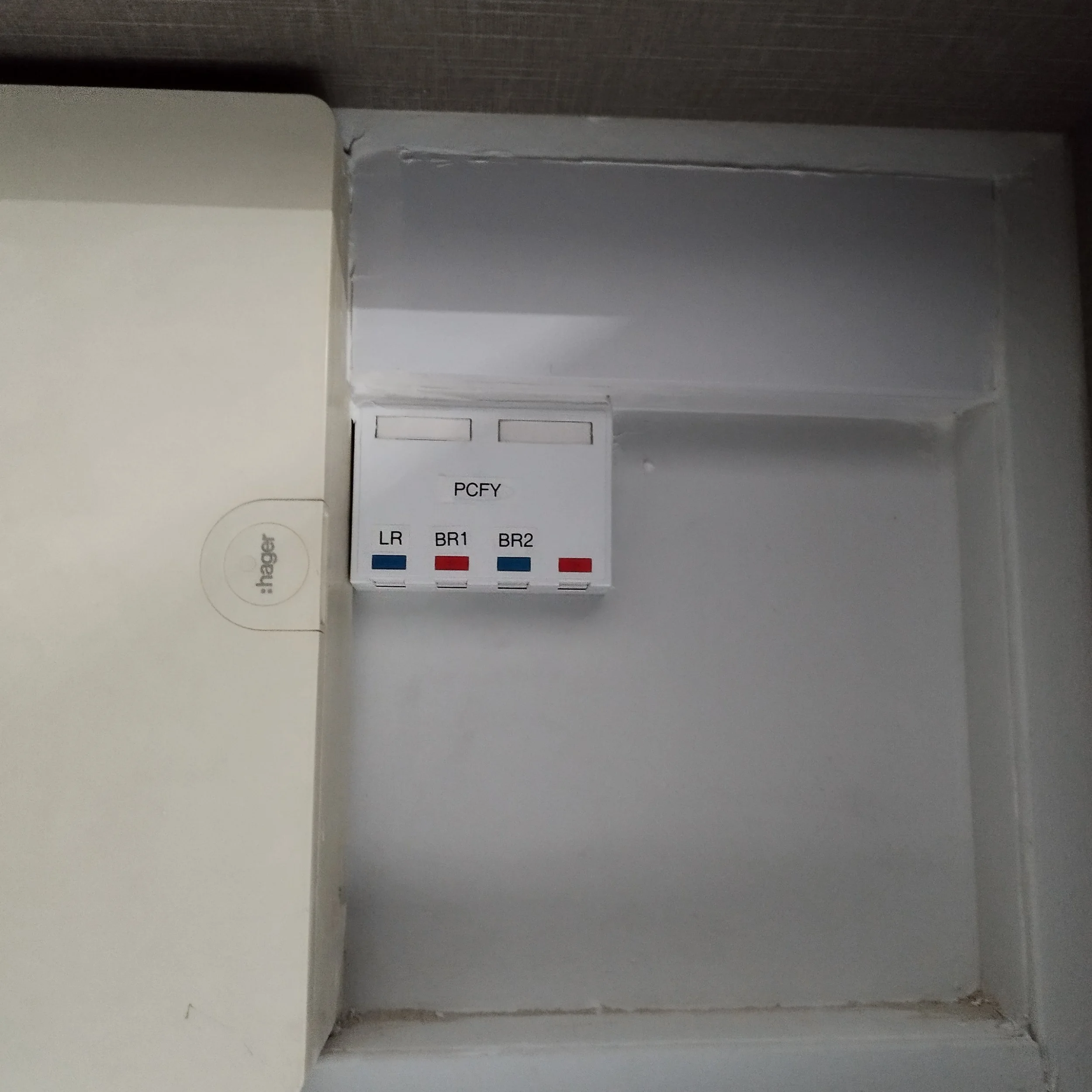 Indoor corner with a white device or box on a white surface, a section of a wall, and a label with color codes and text including 'PCEY', 'LR', 'BR1', and 'BR2' visible below the device.