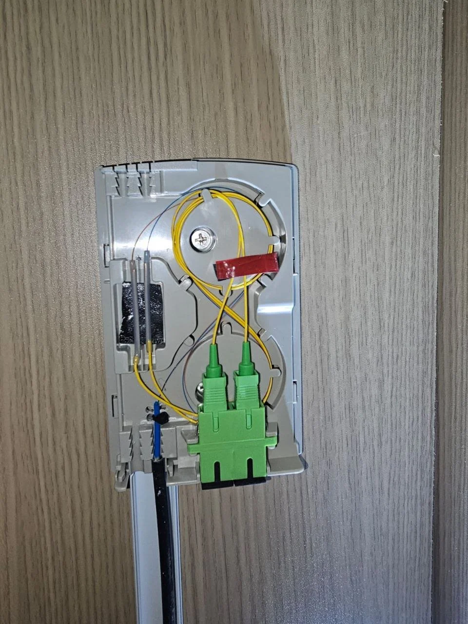 Open wall box with yellow and green wires, plastic mounting bracket, and metal components visible.