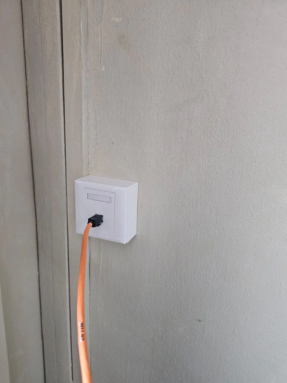 An orange extension cord plugged into an electrical outlet on a beige wall.
