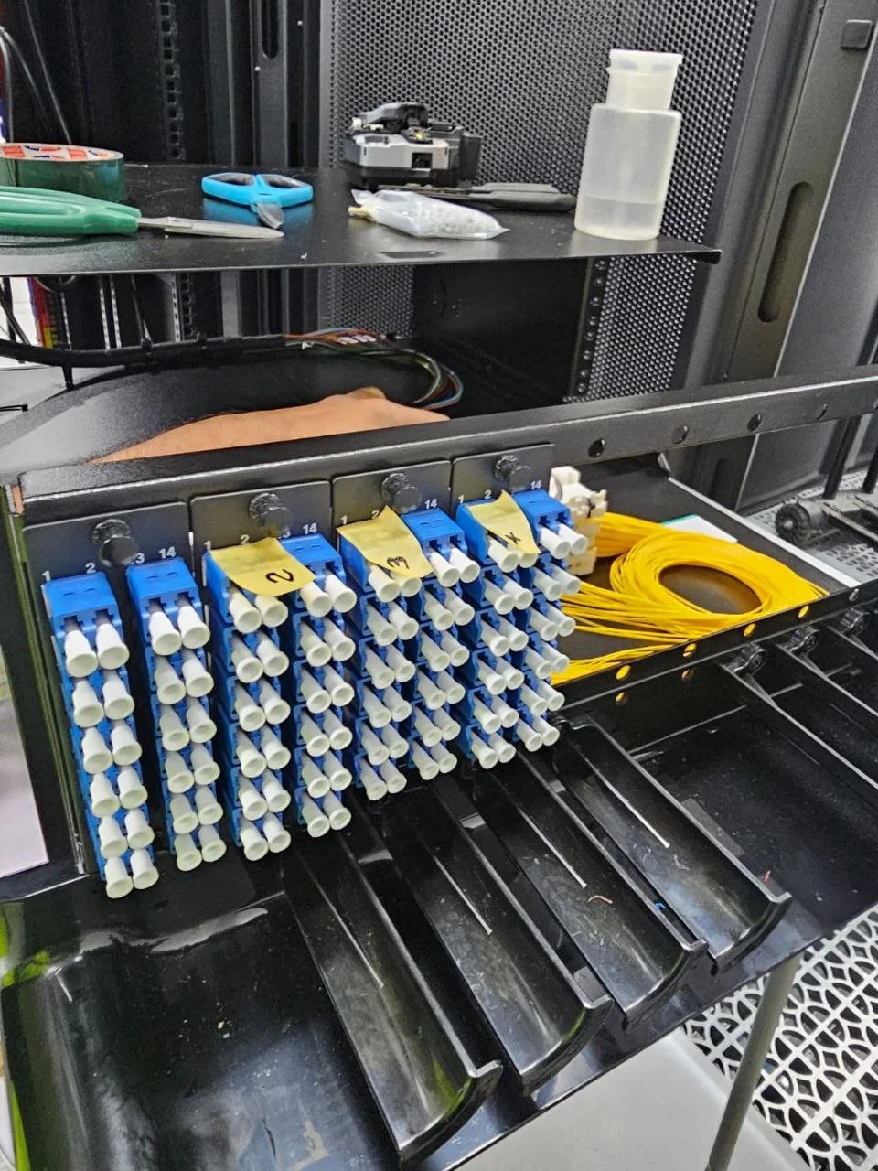 Fiber optic cable management panel with yellow cables and organized blue cable connectors.