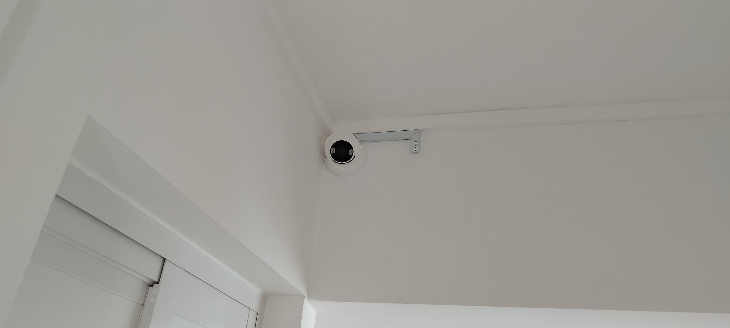A security camera mounted in the corner of a white ceiling.
