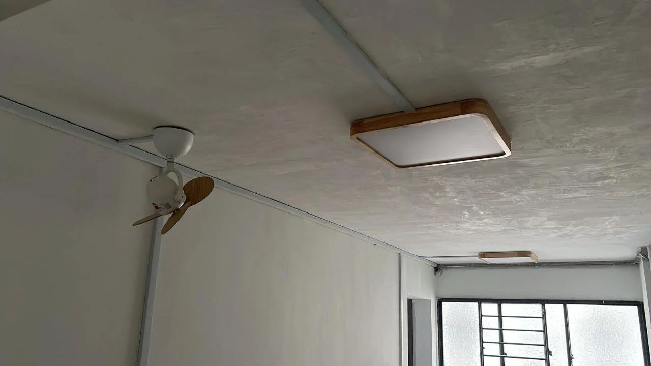 Ceiling with a small ceiling fan with wooden blades and a square flush-mounted ceiling light. Window with bars in the background.