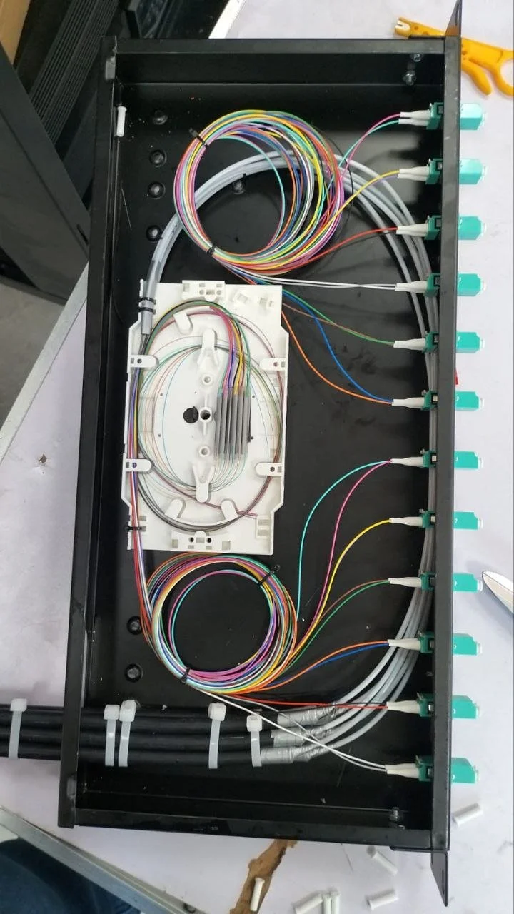 Open fiber optic distribution box with numerous colorful fiber optic cables connected to ports and some cables bundled together inside.