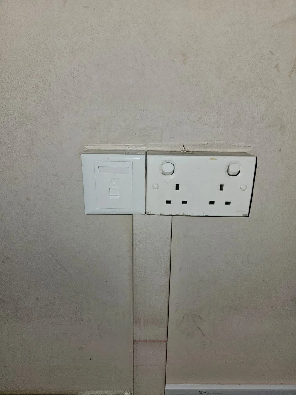 A wall with two electrical outlets, one is a white switch plate and the other is a double wall socket with missing cover plates.