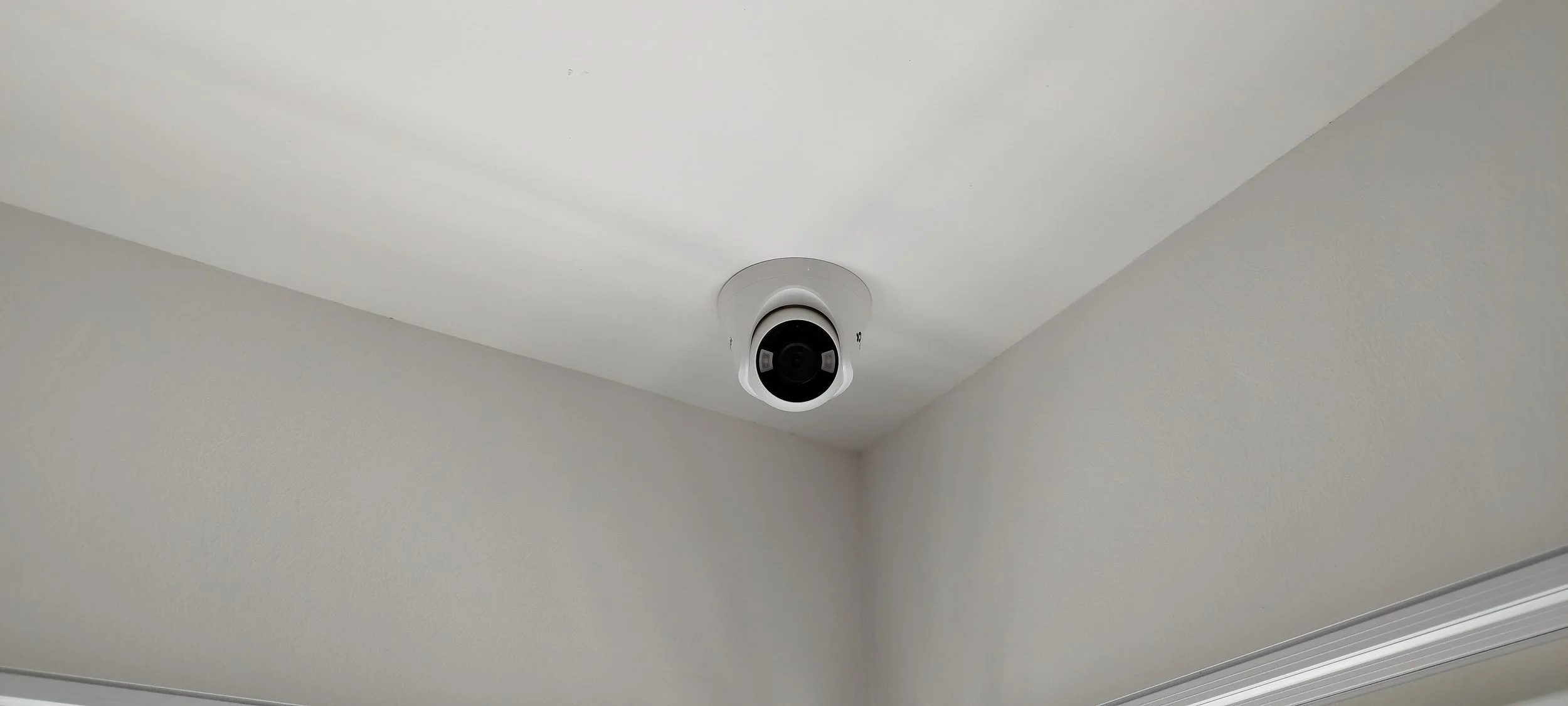 Security camera mounted on the ceiling in a room with white walls.
