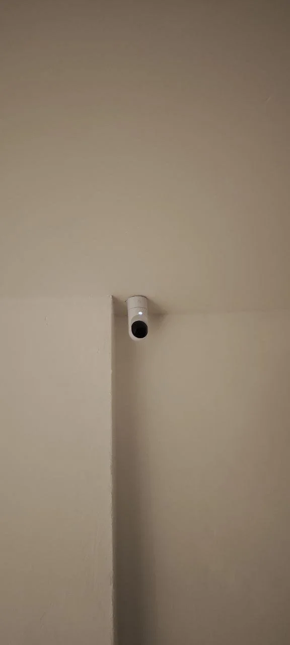 Ceiling-mounted security camera in a room with beige walls.