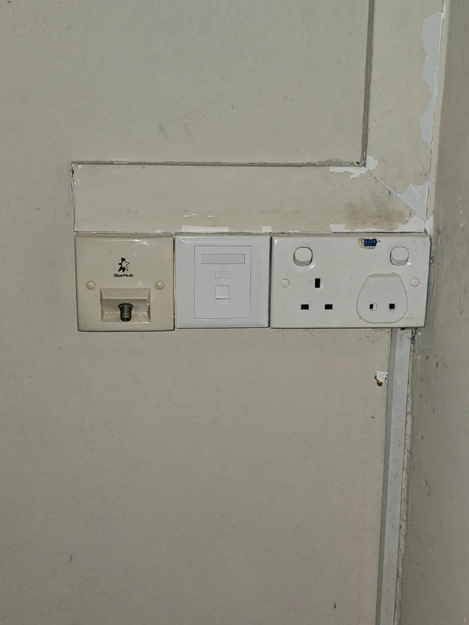 A wall with three electrical outlets, including a USB socket, a telephone socket, and a UK power outlet, with peeling paint and wall damage.