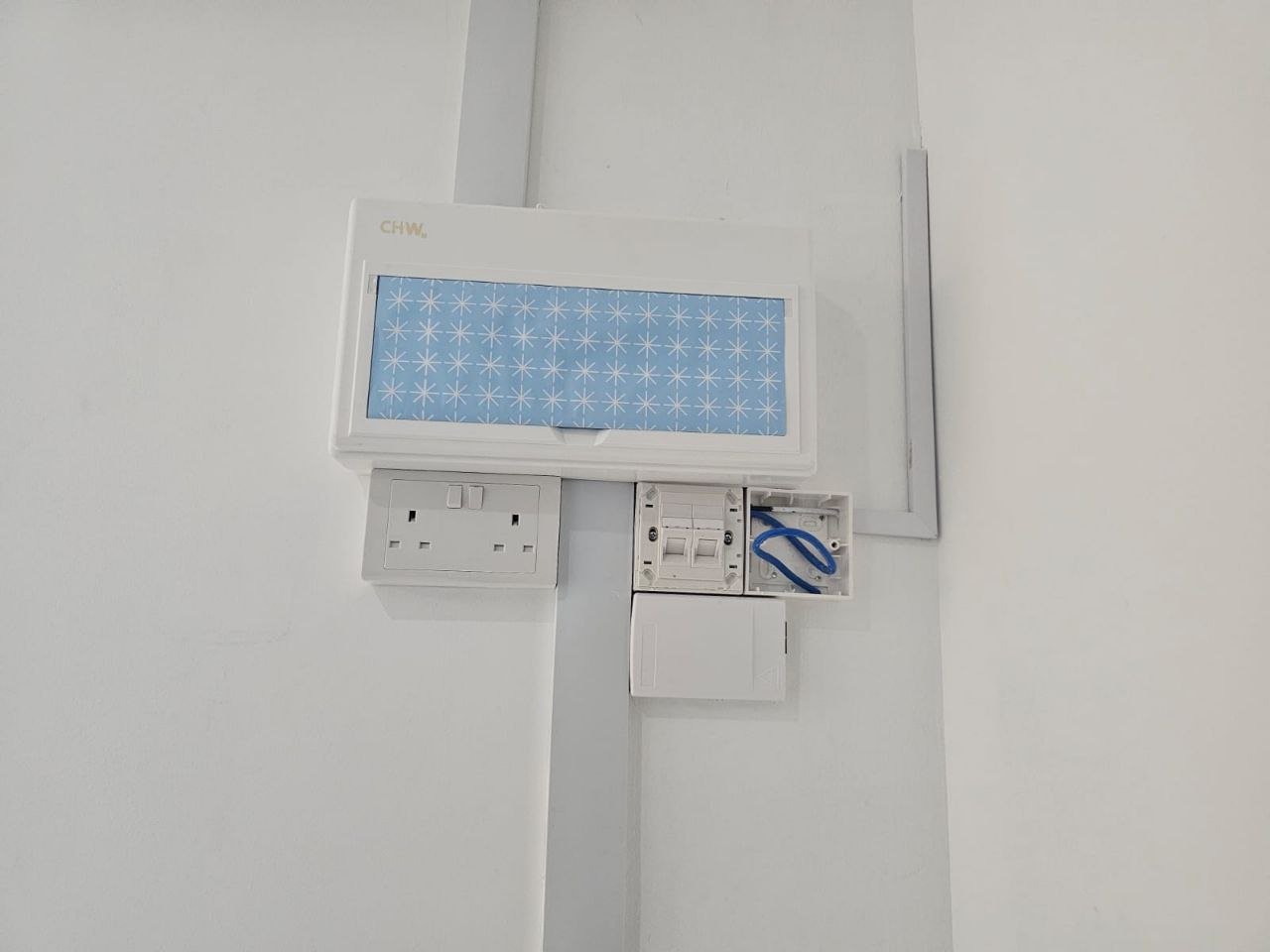 A white electrical panel with a blue star pattern on the cover and an open section with wires, against a white wall.