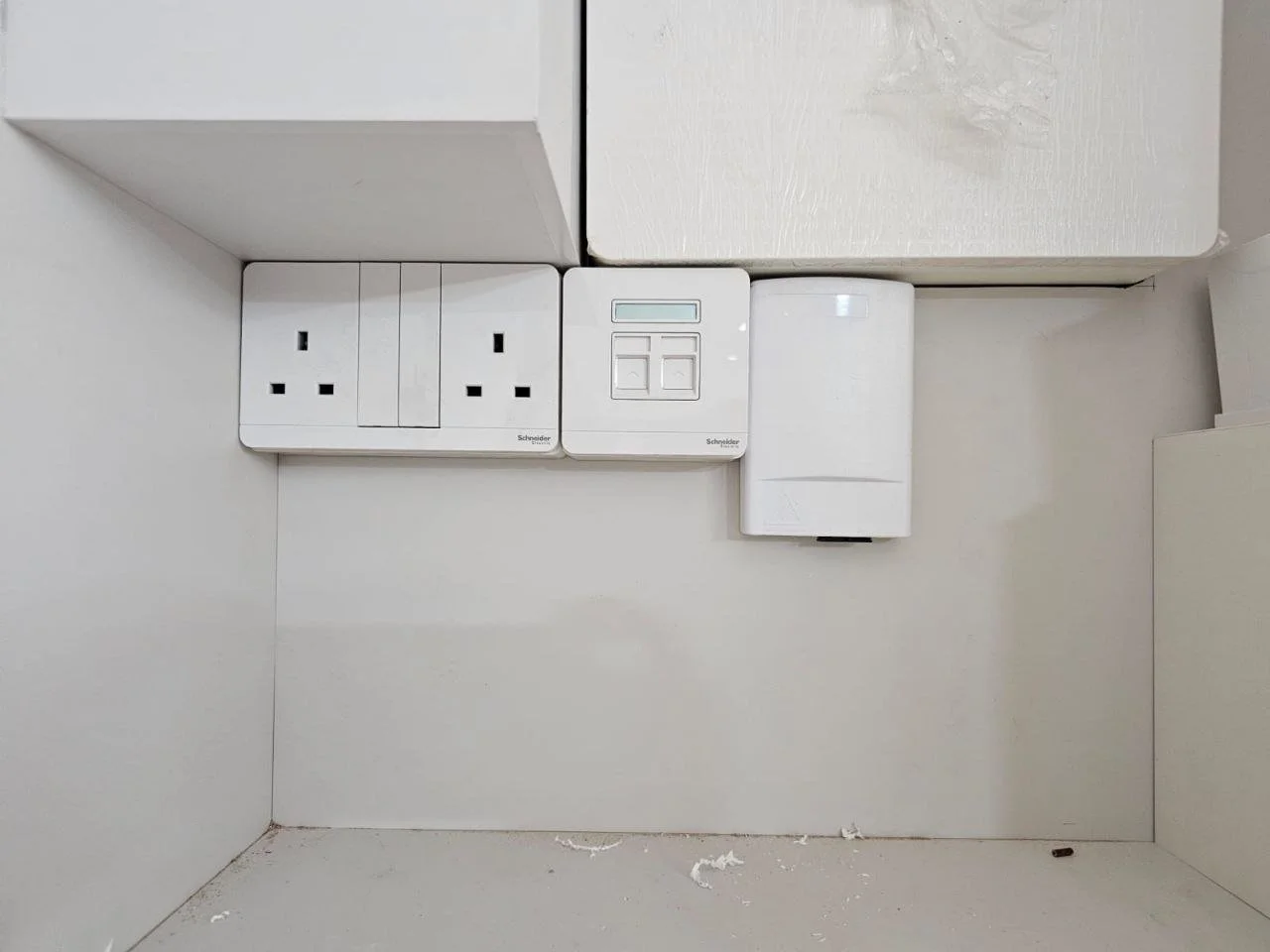 Wall with electrical outlets, switches, and a device, all branded Schneider, on a white wall in a room.