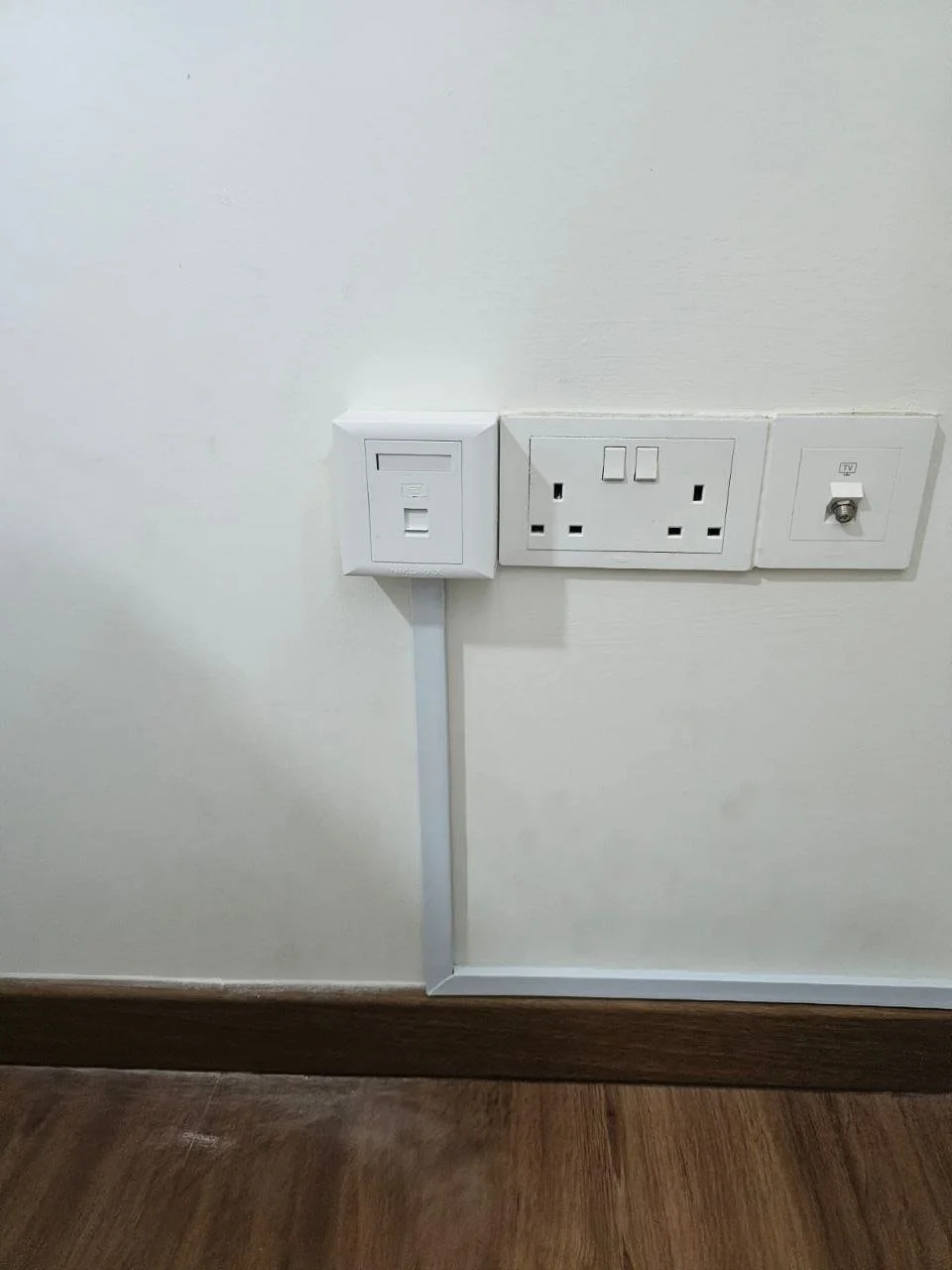 White electrical outlets and switches on a wall, near a wooden floor.