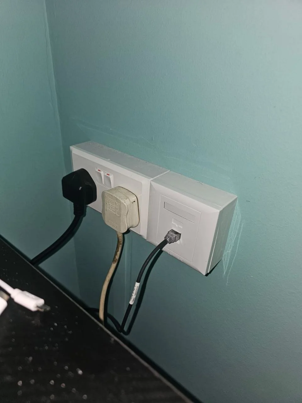 Electrical outlets and power cords plugged into a wall in a room.