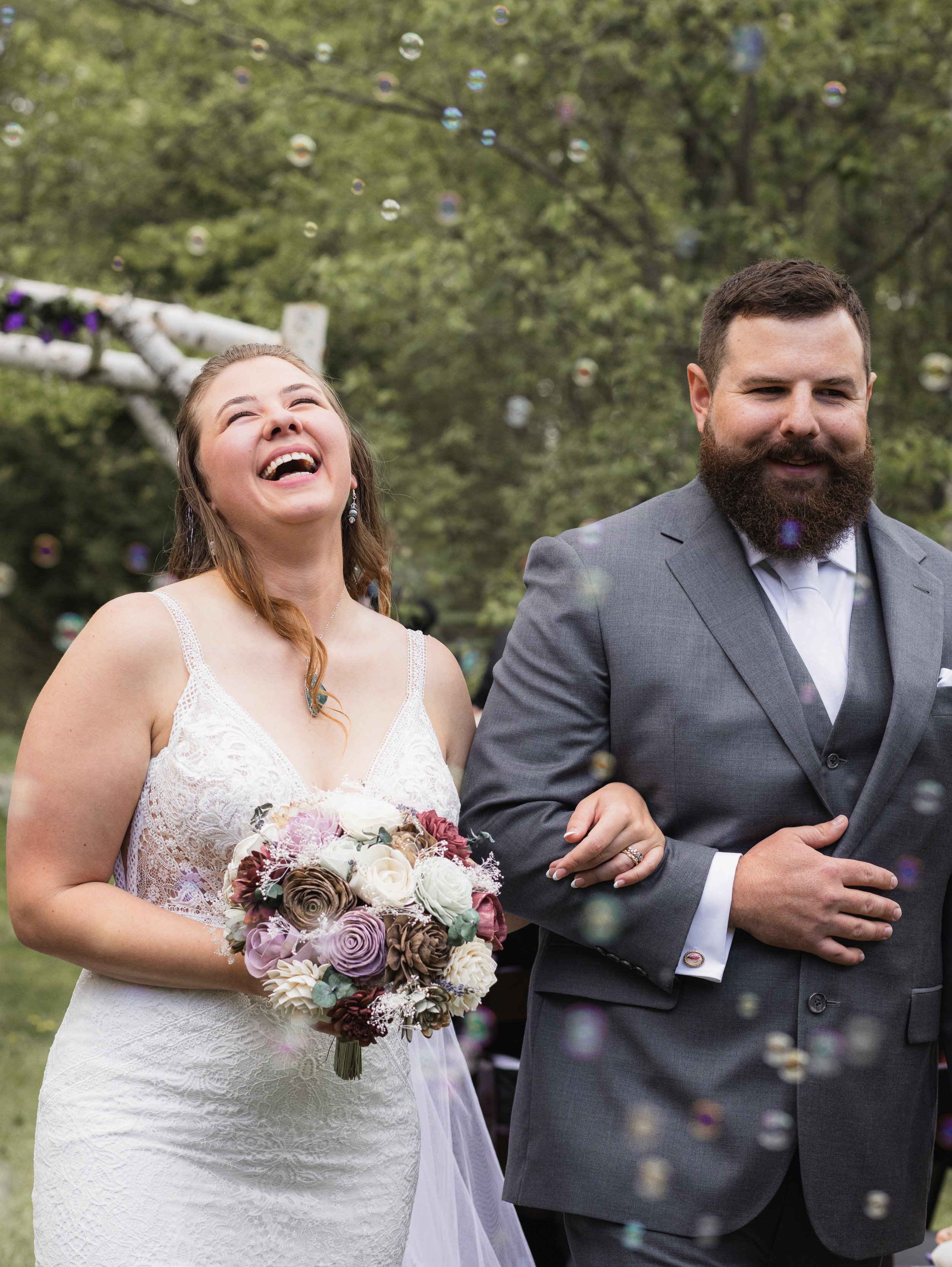 photography of couple walking back through the aisle after getting married with bride laughing as bubbles fill the air