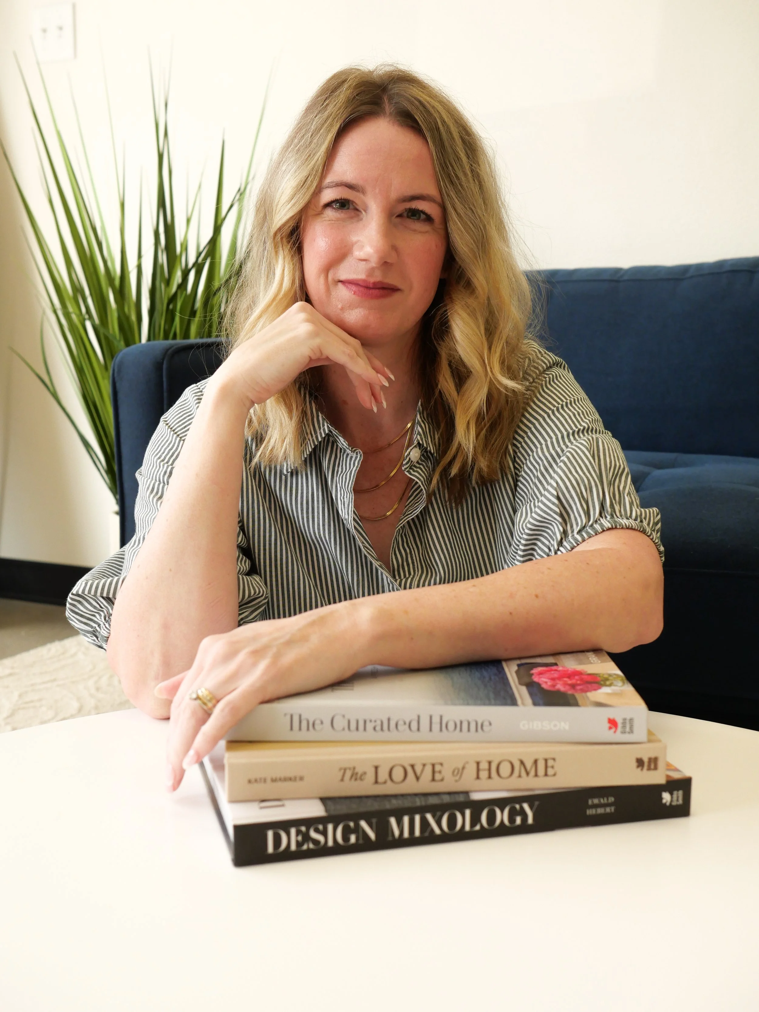 Interior designer and educator Adrienne Meachum seated beside a stack of interior design books.