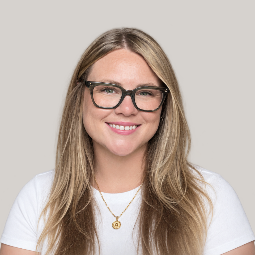 Blonde woman with glasses, white shirt, gold necklace, smiling. Emerge Counseling