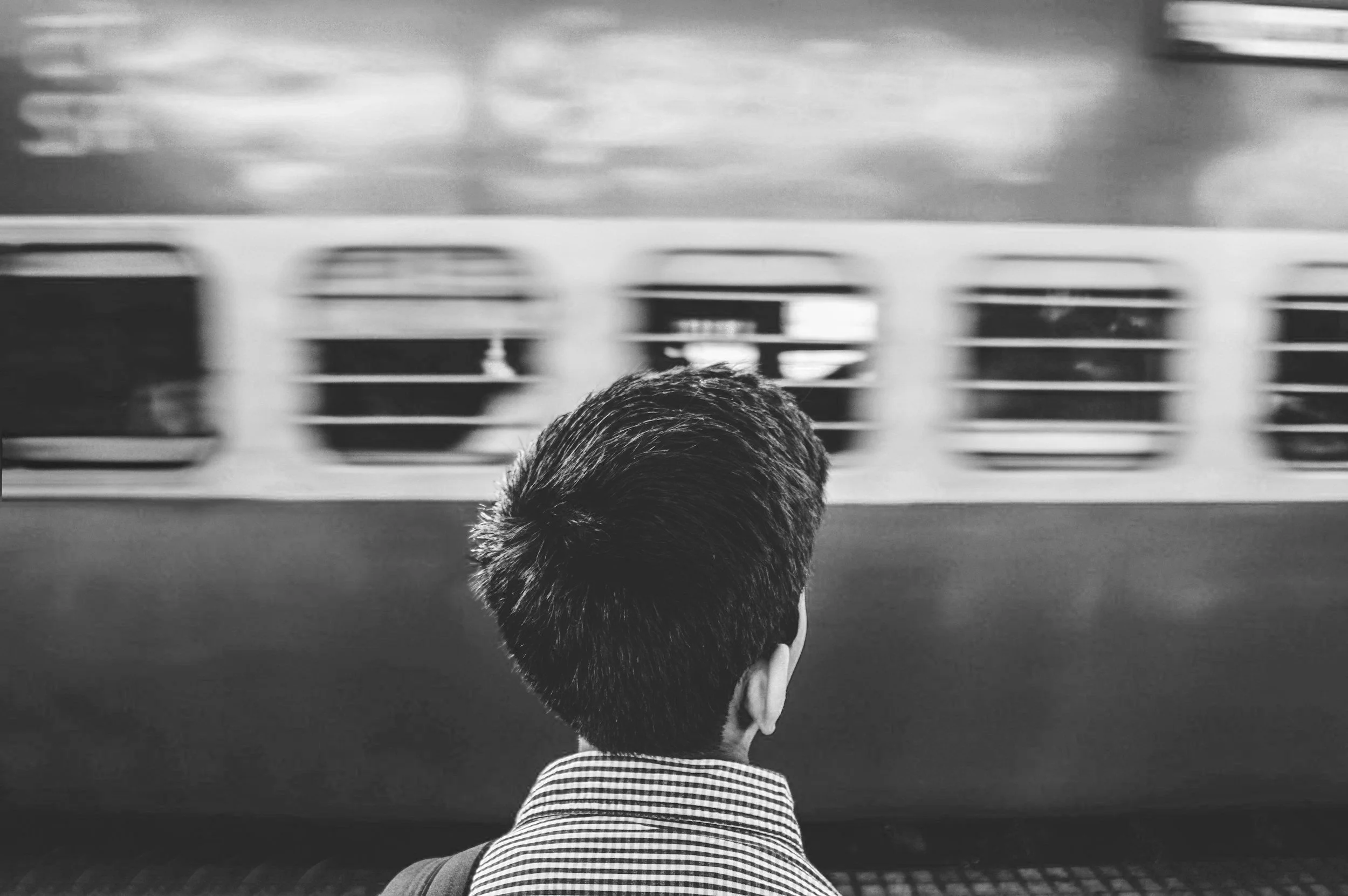 black and white photo of person with short hair looking away from camera at a train passing by