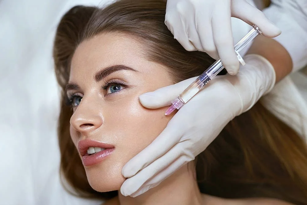 A woman receiving a cosmetic facial injection from a healthcare professional wearing gloves.
