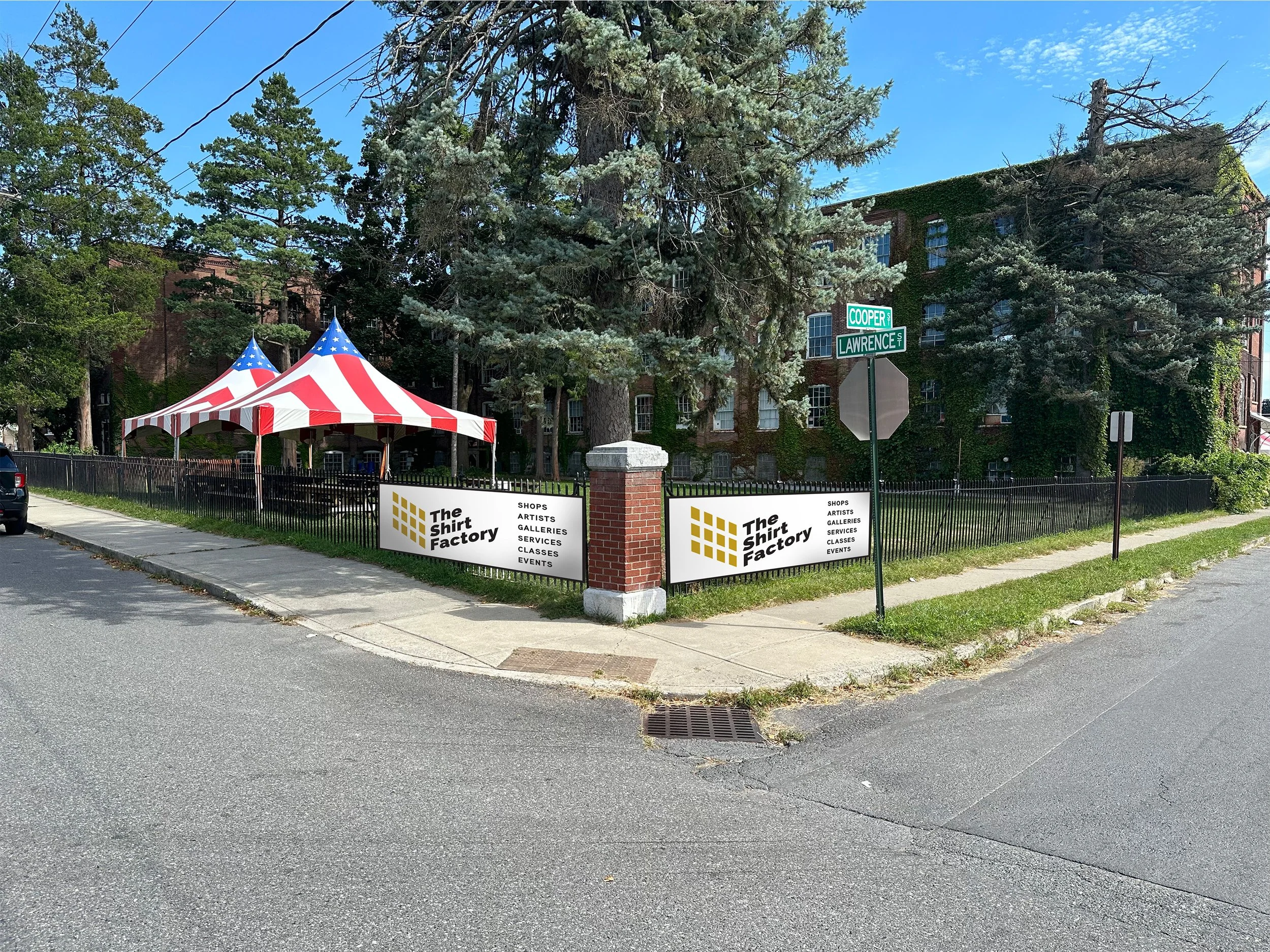 Street view of The Shirt Factory with a red and white striped tent and sign advertising shops, artists, galleries, services, classes, and events.