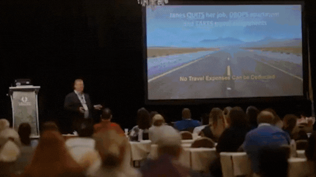 A man giving a presentation at a conference with a slide that reads "Some cities have jobs, some don’t. No Travel Expenses & Low Cost". The audience is seated facing the stage.