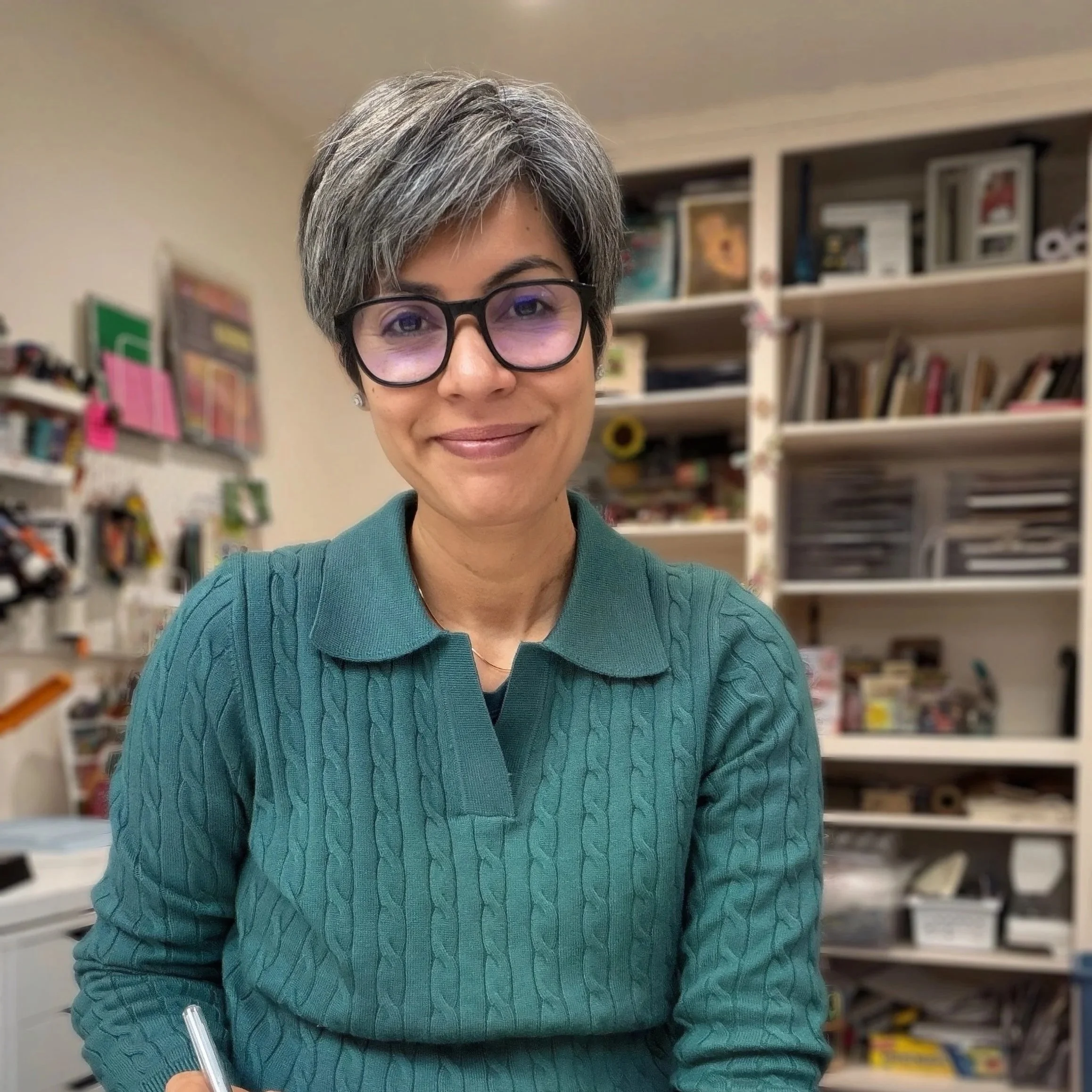 A woman with short brown hair, wearing a maroon top, smiling and looking at the camera with a background that has a white and light gray geometric pattern. The word 'Hello!' is written in black cursive on the left side.