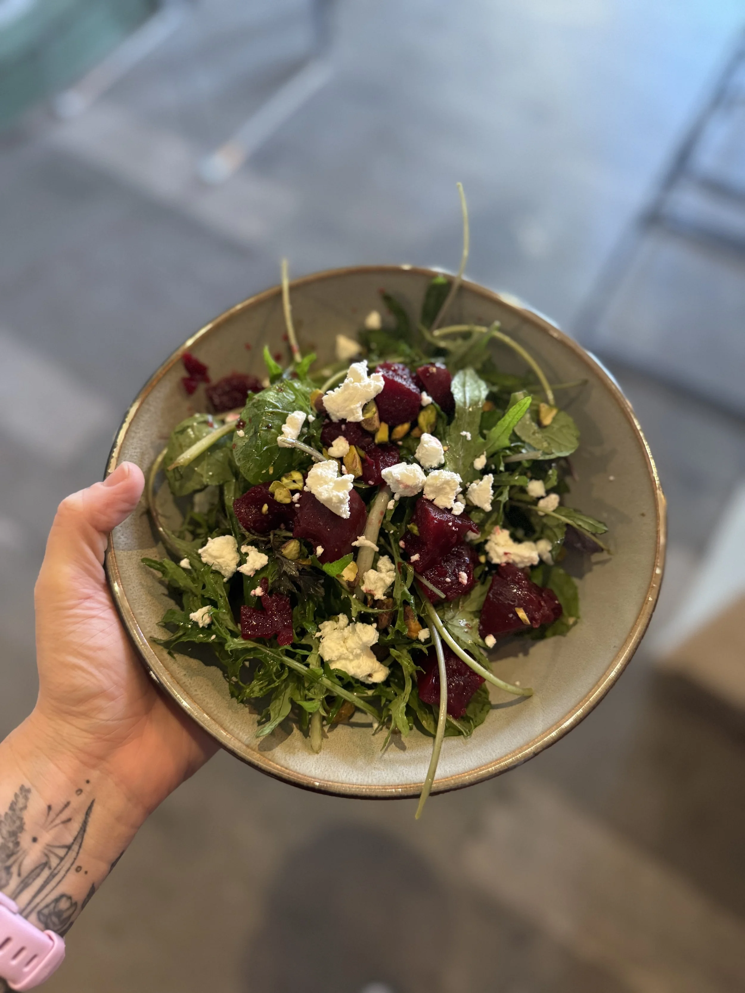 hand holding a salad bowl with greens, beets, chèvre and pistachios