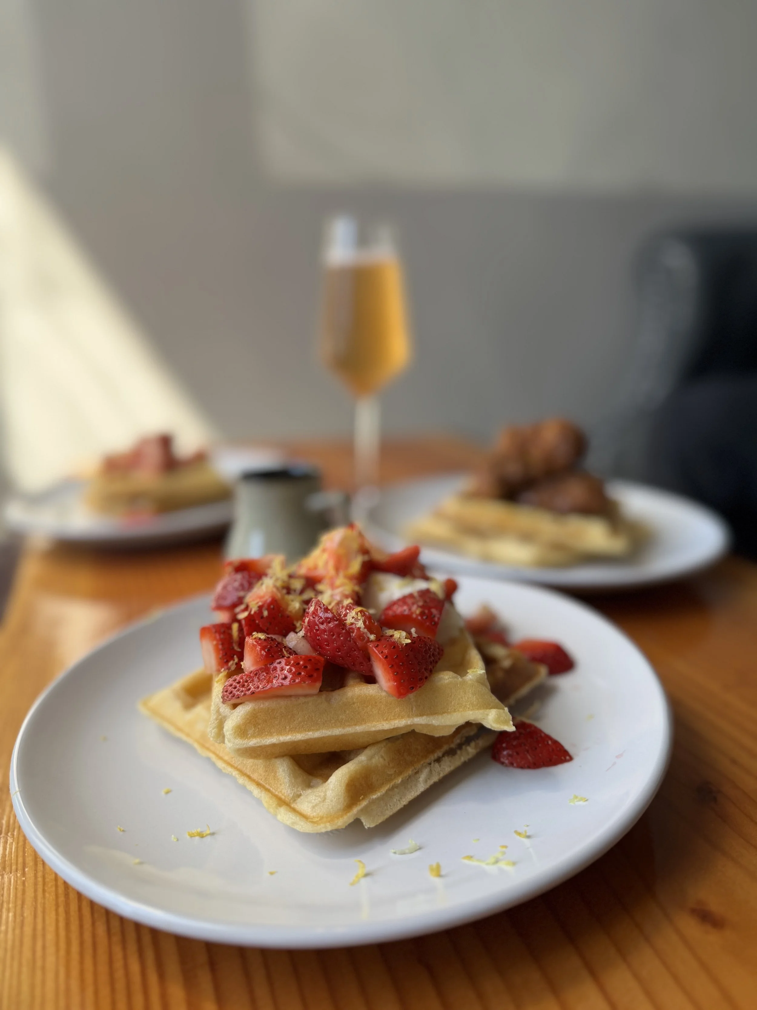 Close-up of a gluten free waffle topped with fresh strawberries and lemon zest on a white plate.